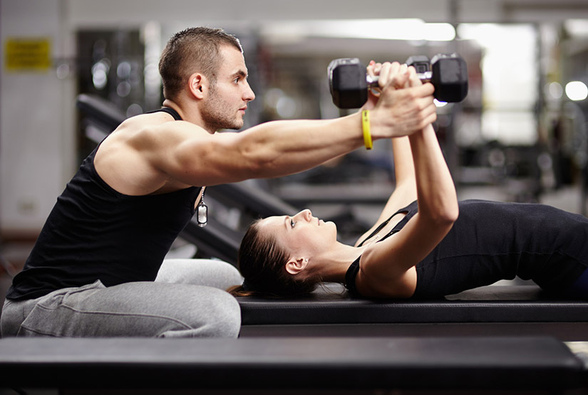 Un personal trainer aiuta una ragazza nell'esecuzione delle croci su panca